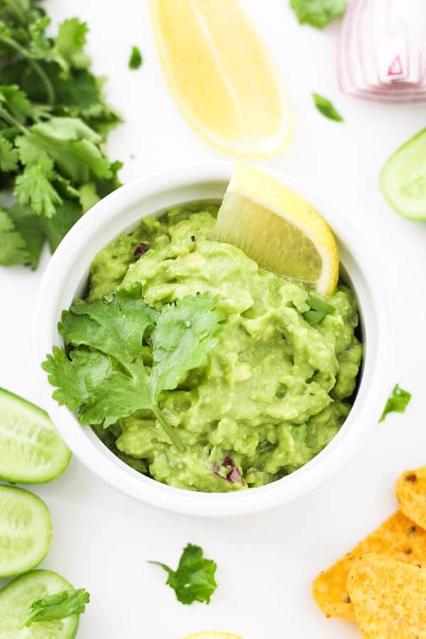 healthy guacamole in a white bowl surrounded by ingredients.
