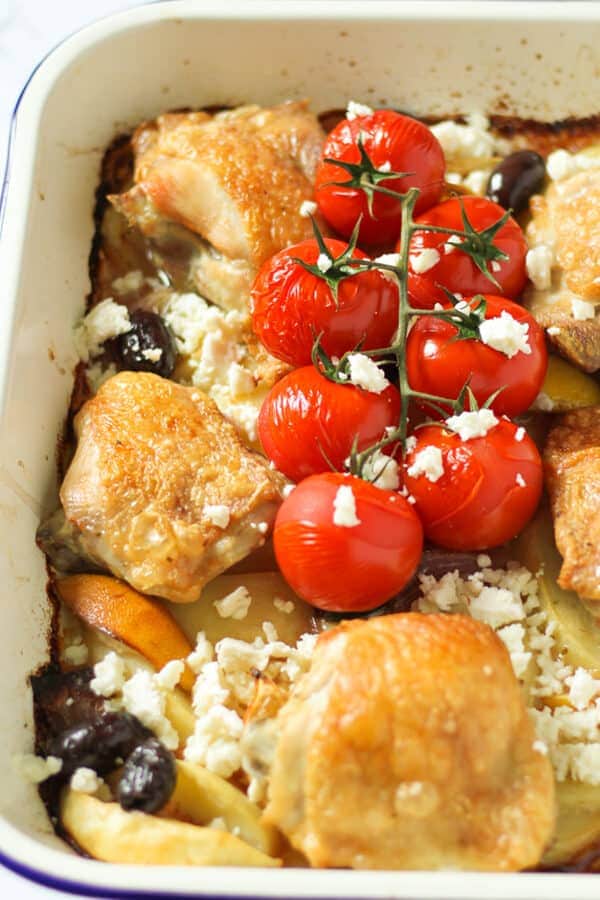 cooked chicken thighs and vegetables in a white tray