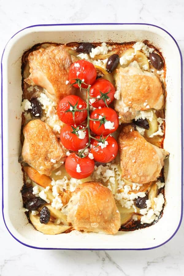 cooked chicken thighs and vegetables in a white tray