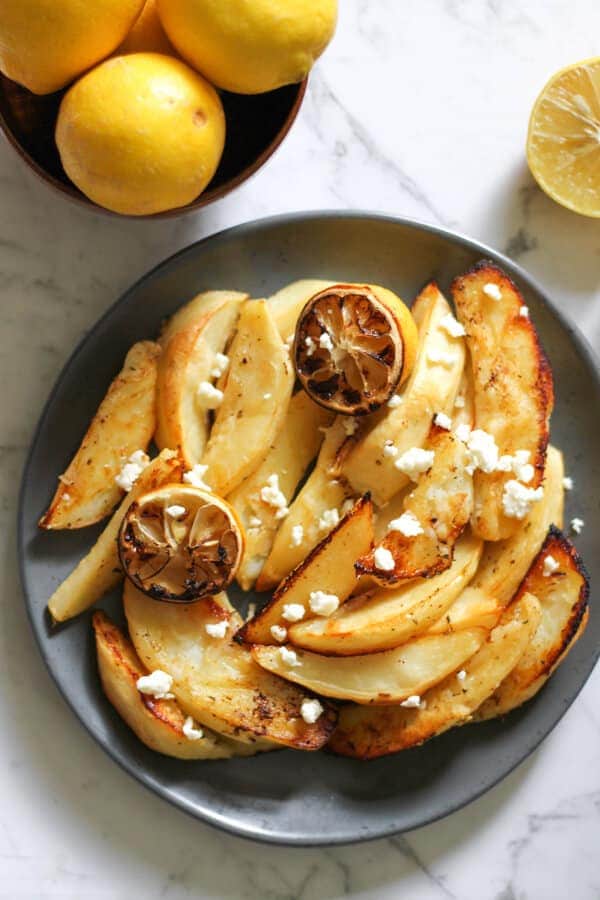 greek lemon potatoes on a grey plate covered in feta cheese 