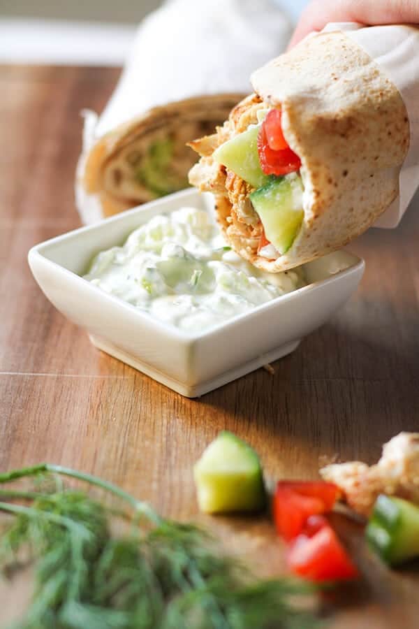 hand dipping chicken gyro wrap into tzatziki.