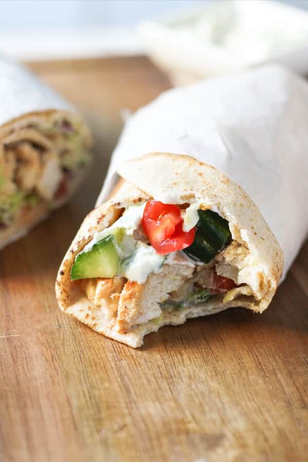 a chicken gyro with a bite removed on a wooden board.