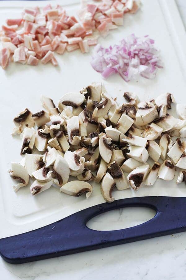 diced bacon, onion and mushrooms on a cutting board.