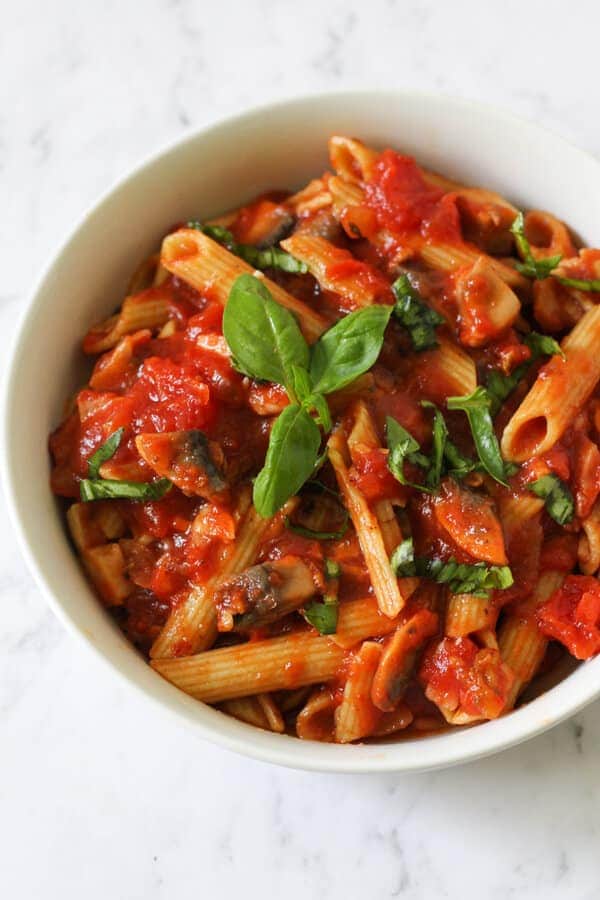 bacon and mushroom pasta in a white bowl topped with basil leaves