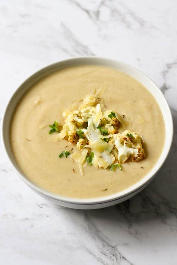 a bowl of cauliflower soup with roasted cauliflower, shredded cheese and parsley on top.