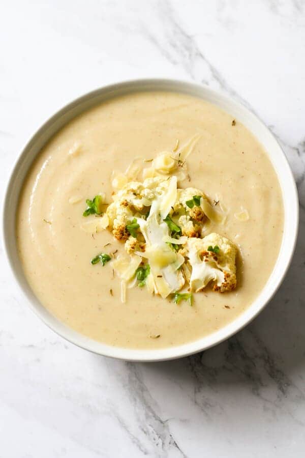a bowl of cauliflower soup with roasted cauliflower, shredded cheese and parsley on top.