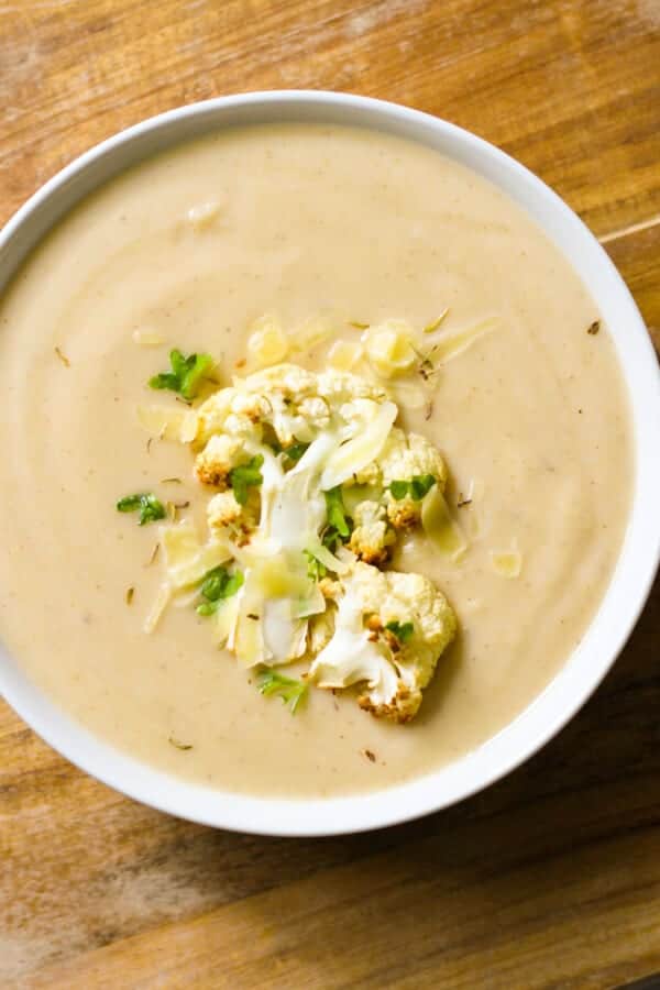 a bowl of cauliflower soup with roasted cauliflower, shredded cheese and parsley on top.