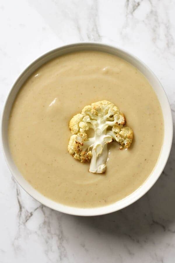 a bowl of cauliflower soup with roasted cauliflower, shredded cheese and parsley on top.