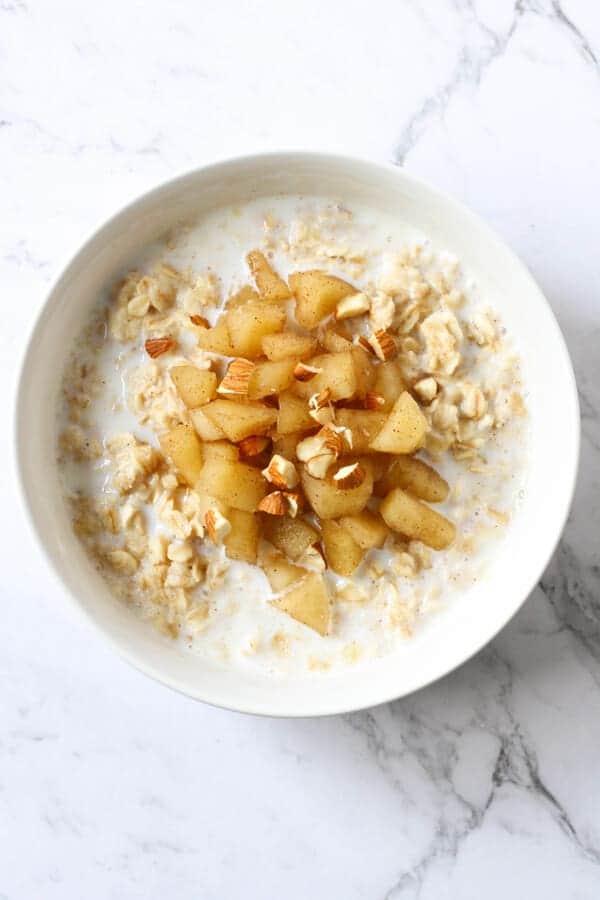 a bowl of oatmeal topped with stewed apple and almonds.