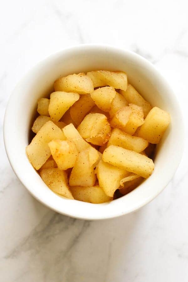 stewed cinnamon apple pieces in a white bowl.