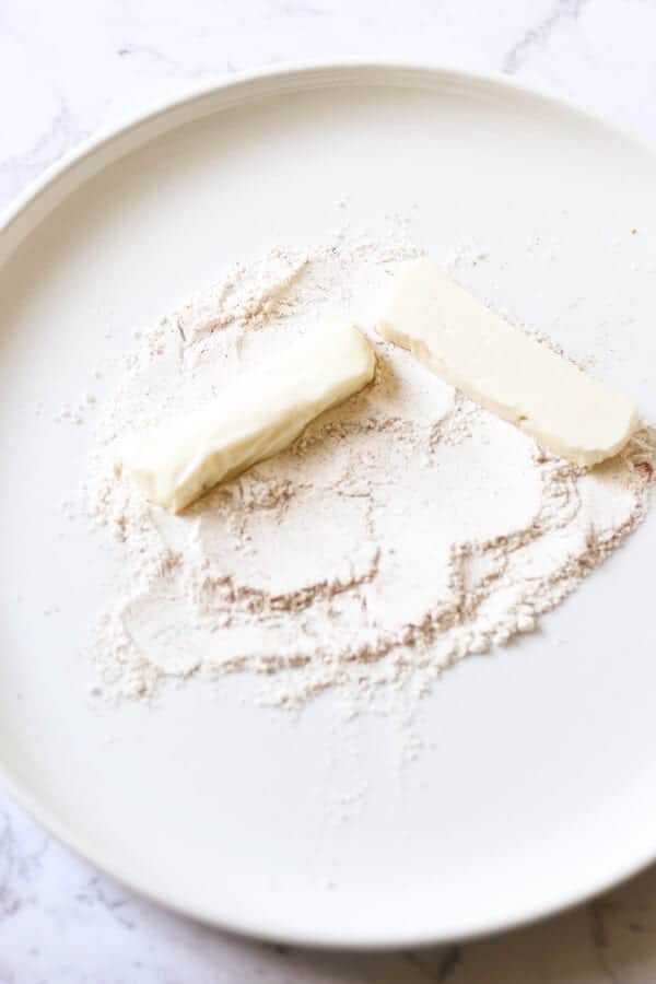 halloumi slices being covered in flour on a white plate.