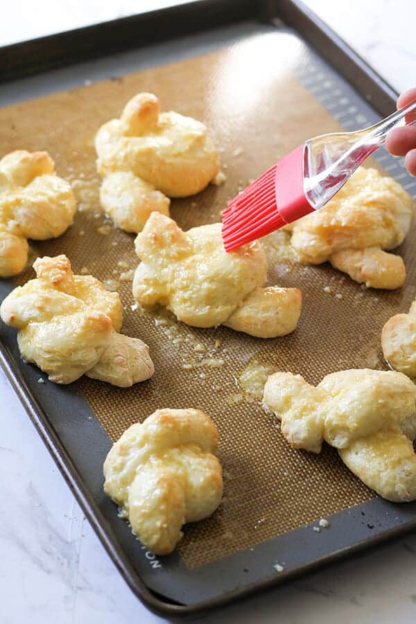 garlic knots on a baking tray being brushed with garlic butter.