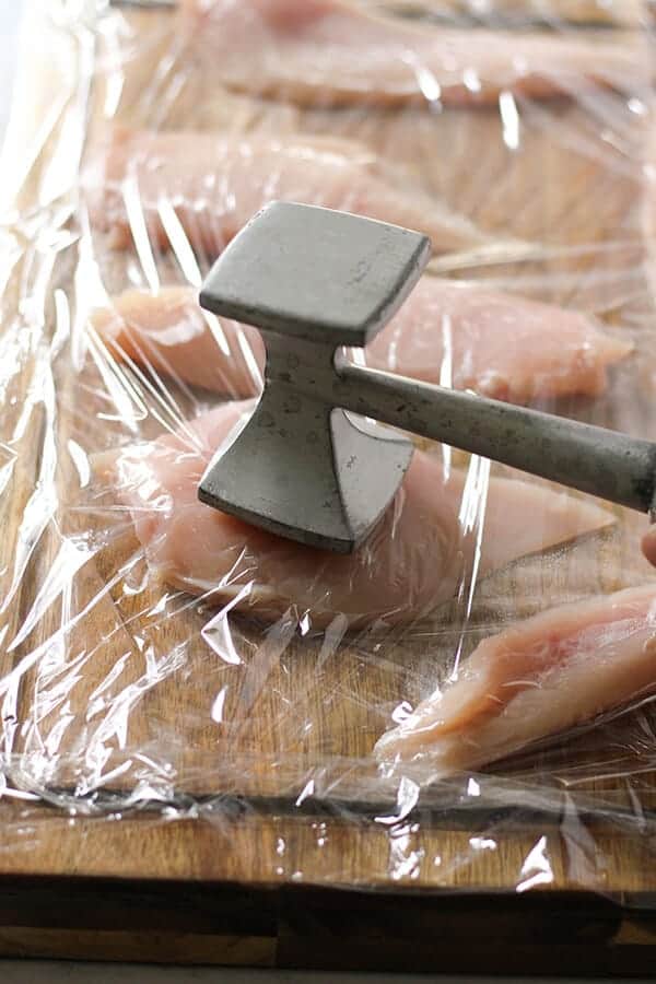 chicken breast on a wooden cutting board being tenderised with a meat mallet.