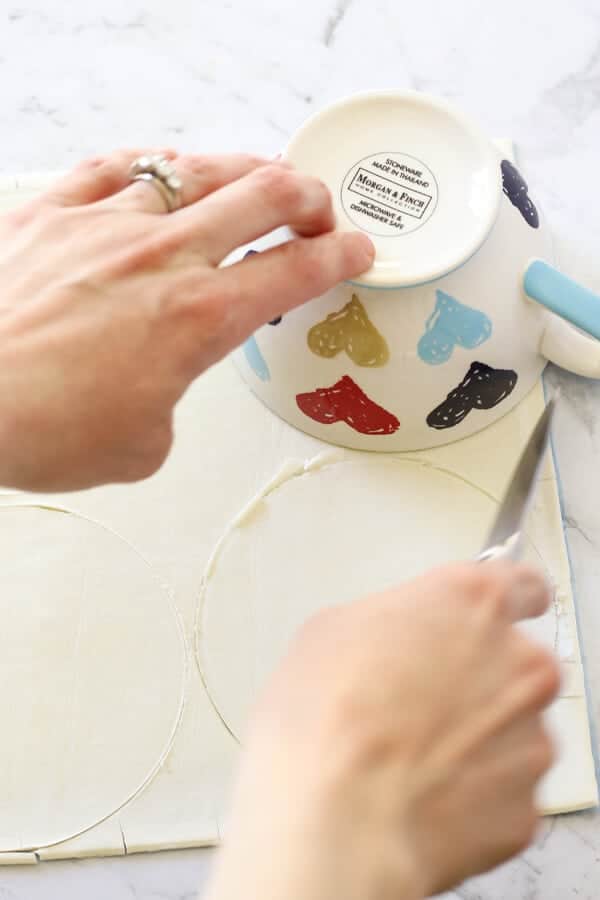 Hand cutting out rounds in a puff pastry sheet.