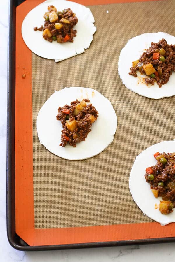 puff pastry rounds on a baking tray with savoury mince in the middle.