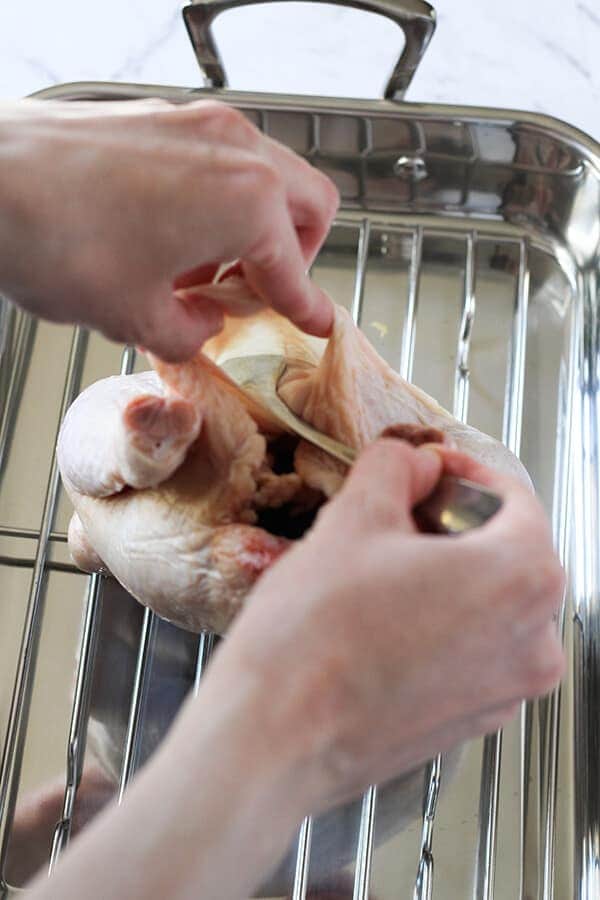 hand using dessert spoon to seperate skin from chicken breast.