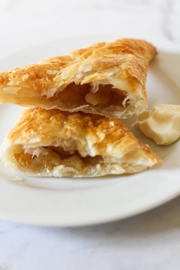 apple turnover broken into halves on a white plate.