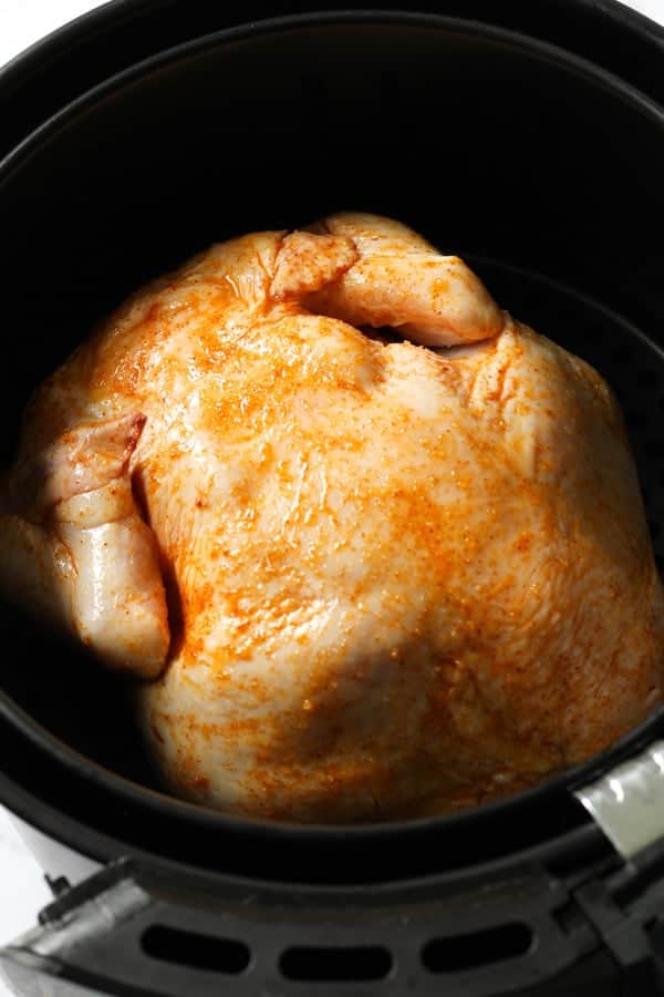 chicken sitting in air fryer basket ready to be roasted.