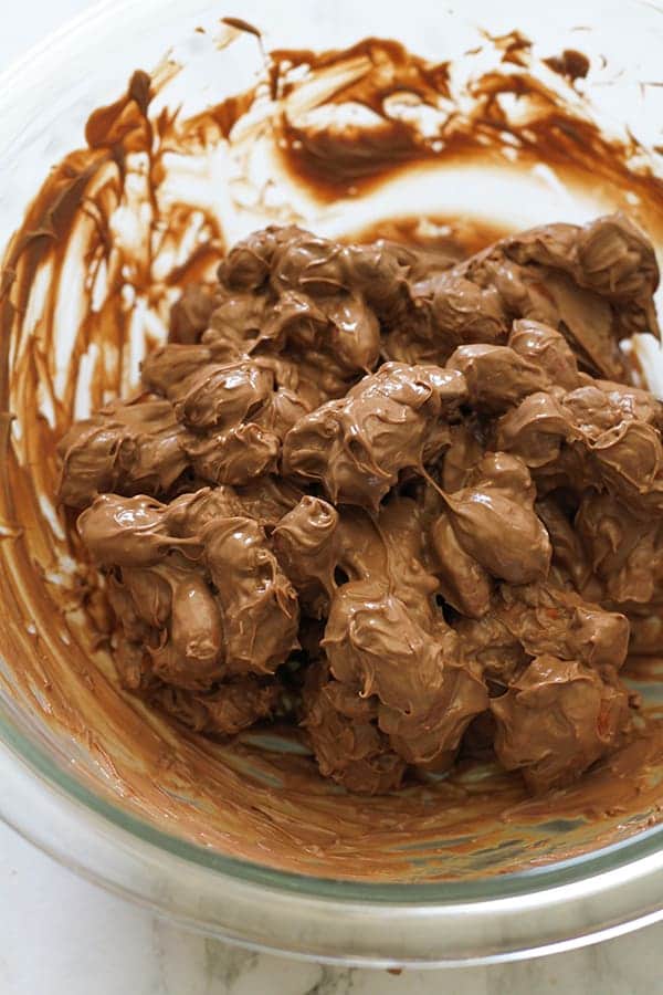 almonds covered in melted chocolate in a glass bowl.