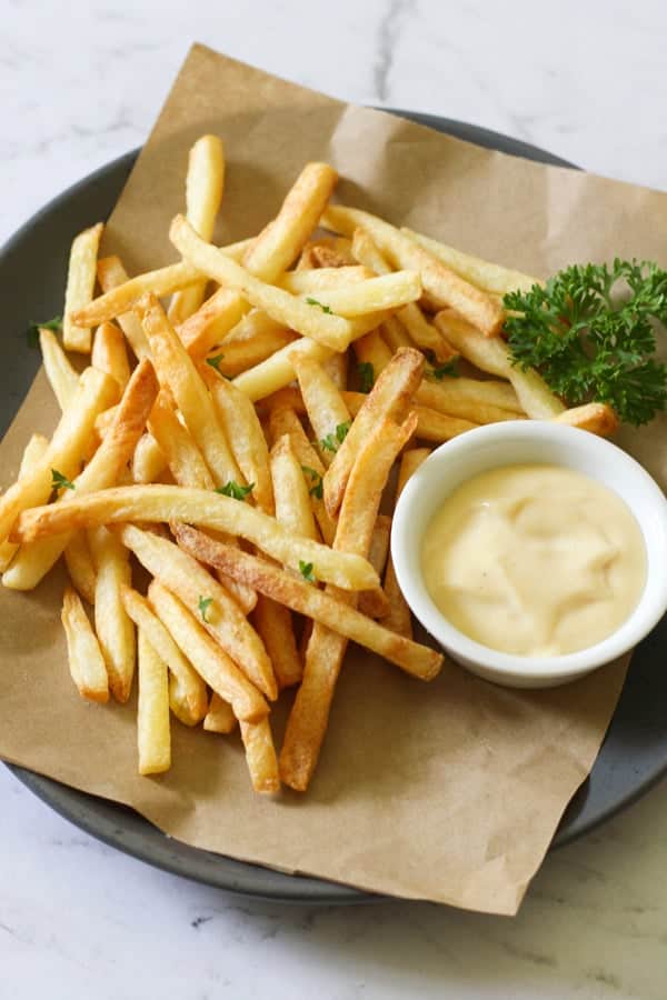 frozen French fries on a grey plate with a bowl of aioli. 