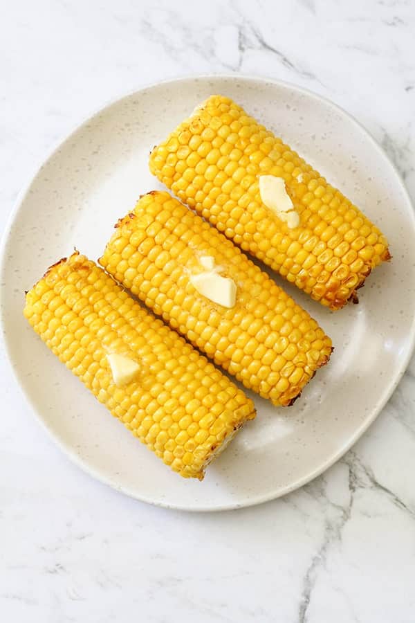 3 corn on the cob on a white plate. 