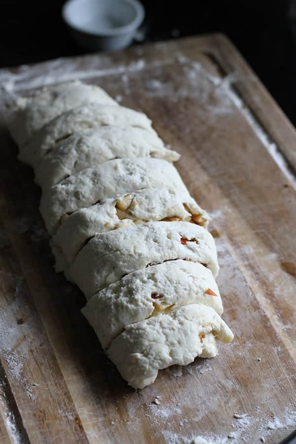 apple cinnamon rolls being cut on a wooden board.