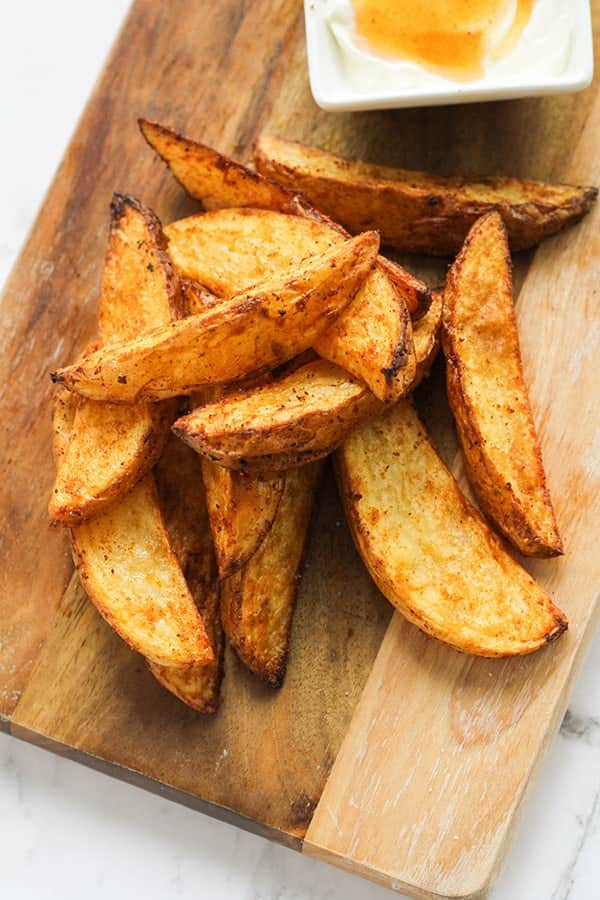 Air fryer potato wedges and dipping sauce on a wooden cutting board.