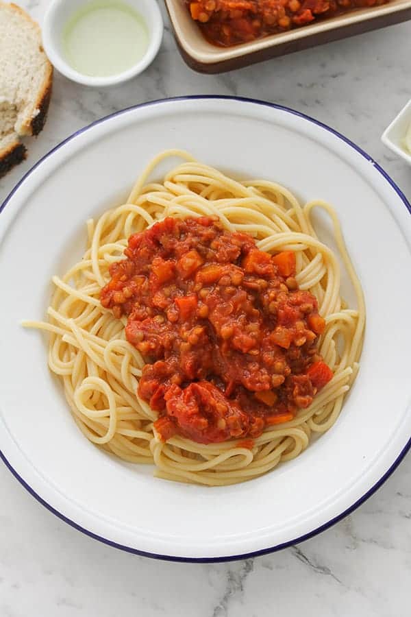 lentil bolognese on top of spaghetti on a white plate.