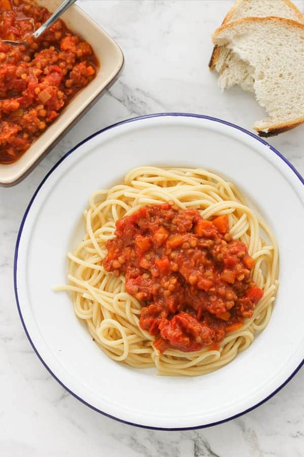 lentil bolognese on top of spaghetti on a white plate.