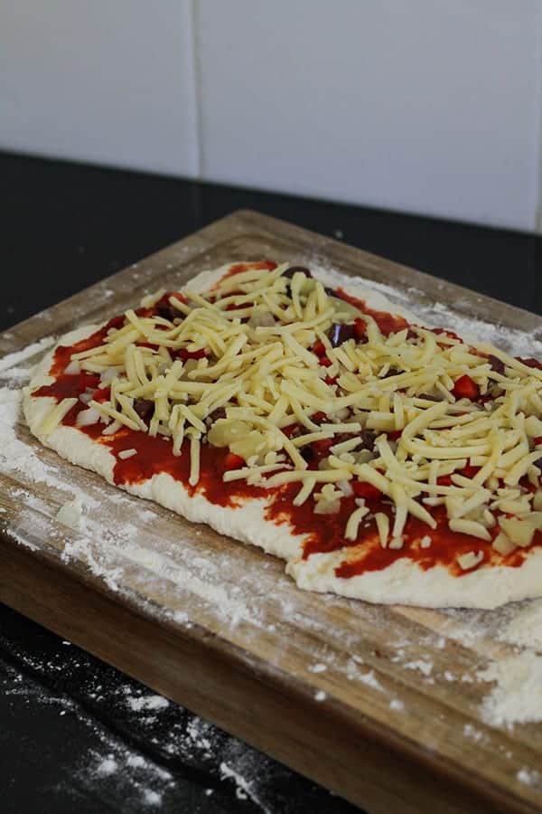 dough covered with toppings on a wooden board.