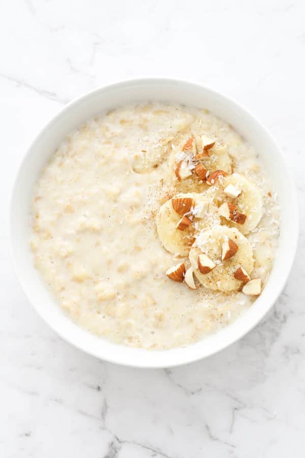 porridge in a white bowl topped with banana slices, cinnamon, almonds and coconut.