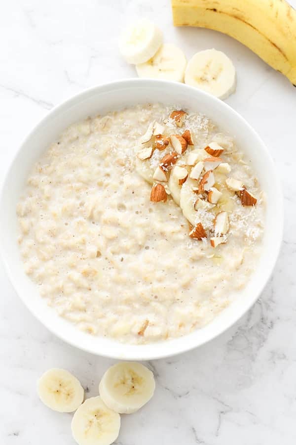 porridge in a white bowl topped with banana slices, cinnamon, almonds and coconut.