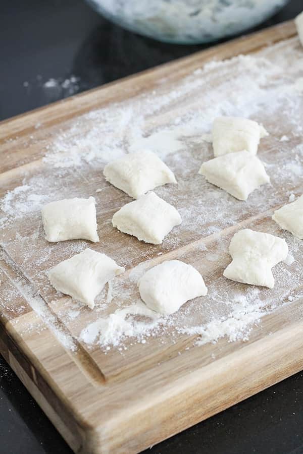 dough cut into bite-sized pieces on a wooden cutting board.