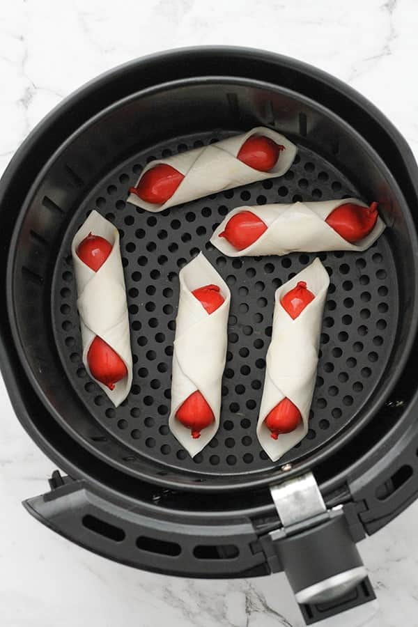 cocktail frankfurts wrapped in puff pastry in an air fryer basket.