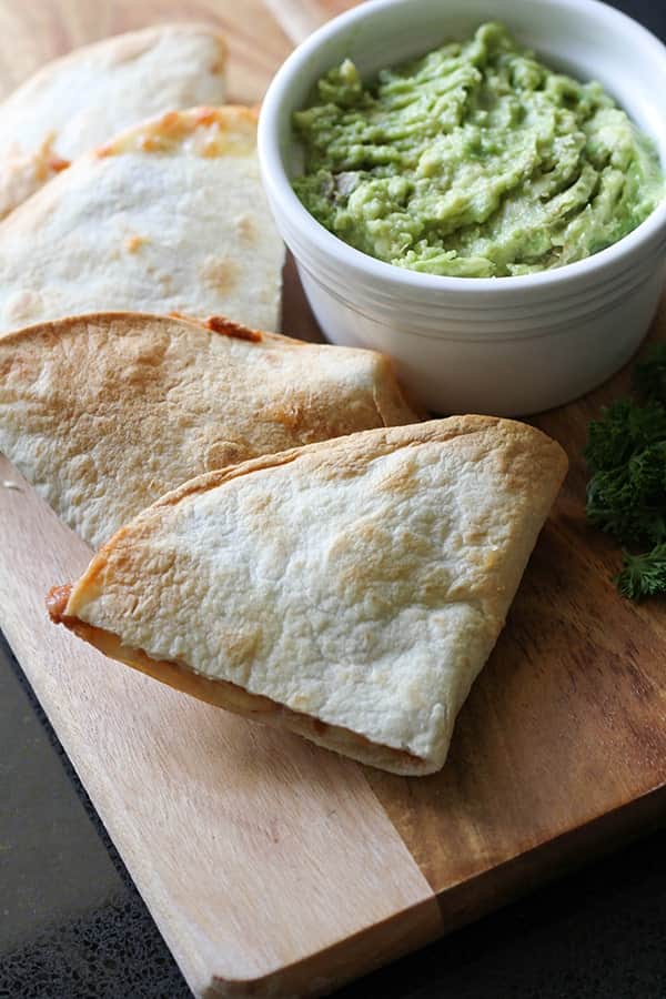 quesadilla quarters on a wooden board with a bowl of guacamole.