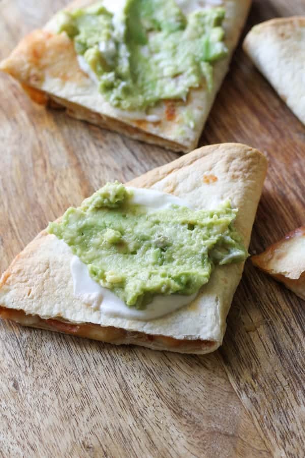 quesadilla quarters on a wooden board topped with guacamole and greek yoghurt.