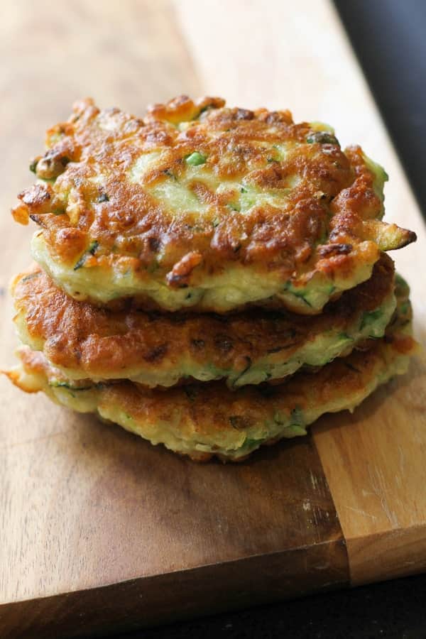 pea & feta fritters stacked on top of each other on a wooden board.