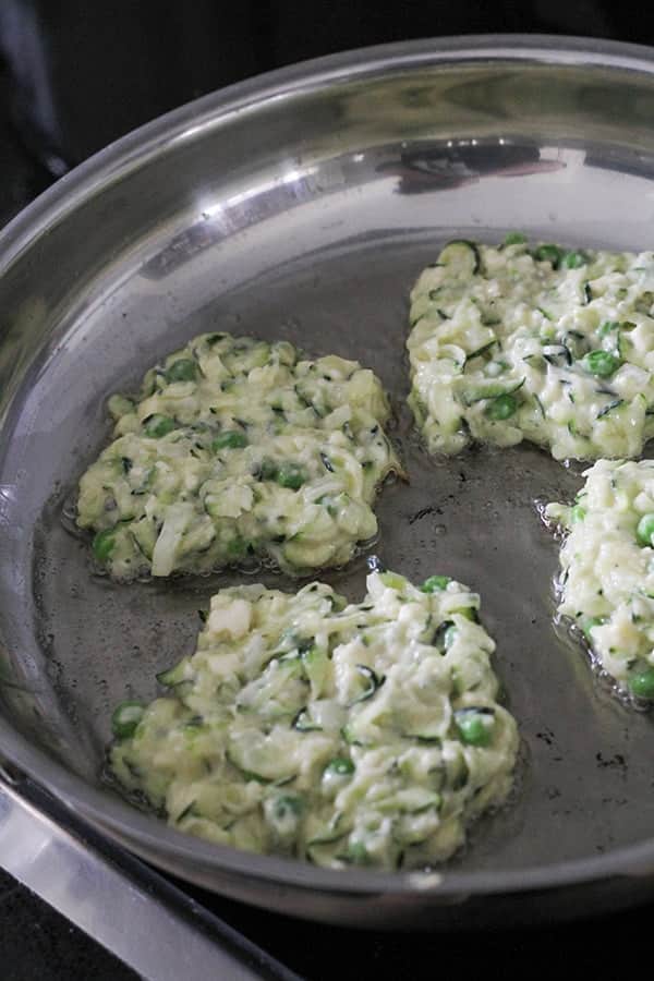 fritters frying in a stainless steel frying pan.