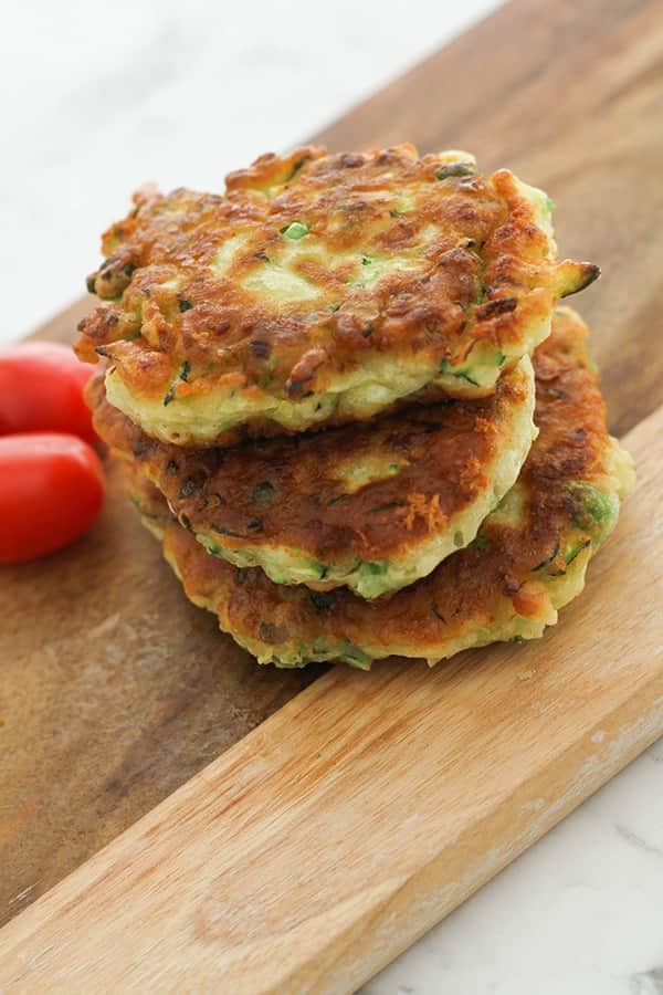 pea & feta fritters stacked on top of each other on a wooden serving board. 