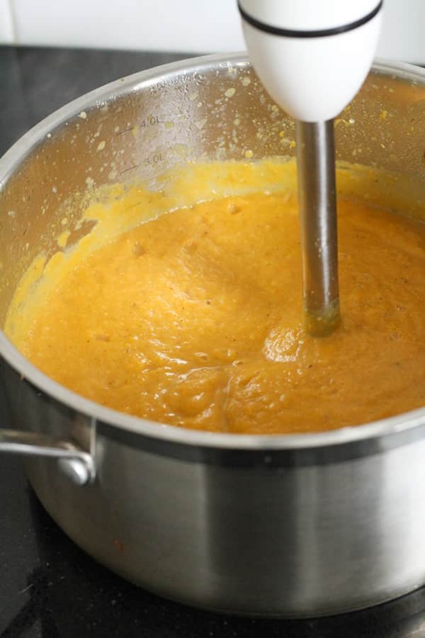 pumpkin and cauliflower soup in a large pot with an immersion blender in the middle of the pot.