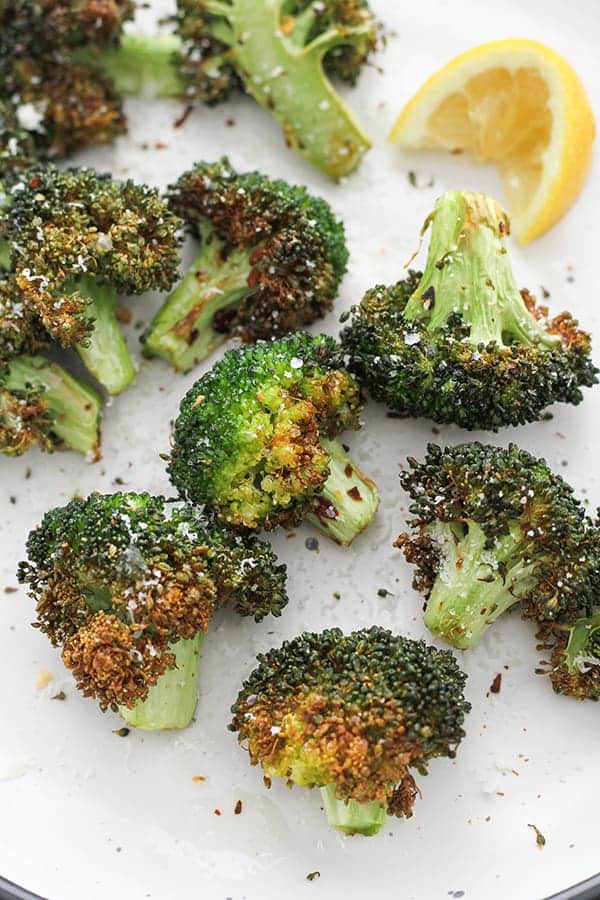 roasted broccoli on a white plate with lemon wedges.