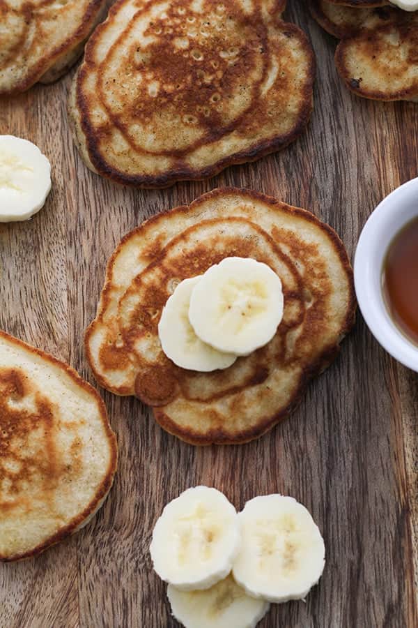pikelets spread out across a wooden board, topped with banana.