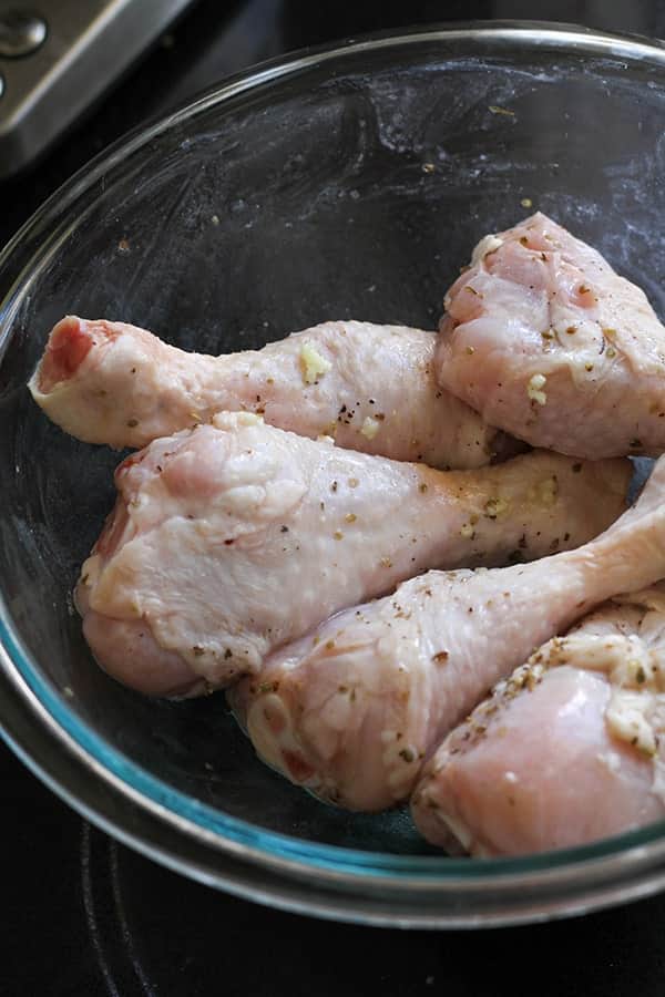chicken drumsticks marinating in a glass bowl.