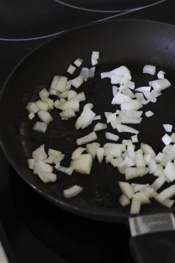 diced onion being sautéed in a skillet.