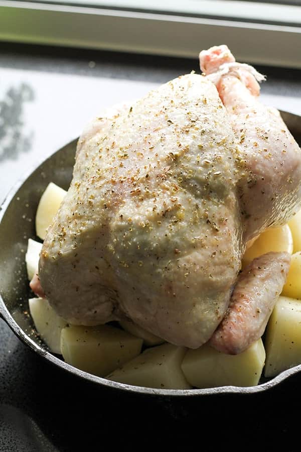 whole chicken and potatoes in a cast iron pan.