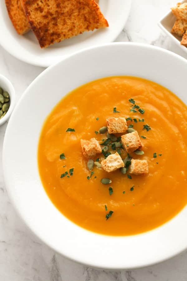 pumpkin soup in a white bowl topped with croutons and pumpkin seeds.