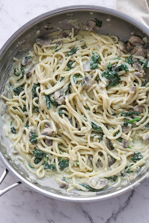 creamy spinach and mushroom pasta in a frying pan.
