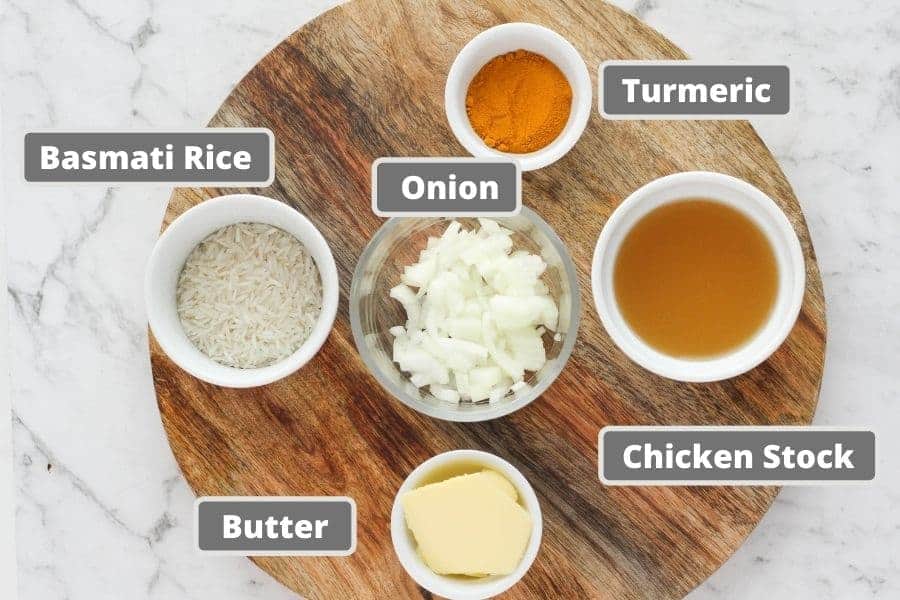ingredients for turmeric rice on a wooden board, including rice, butter and chicken stock.