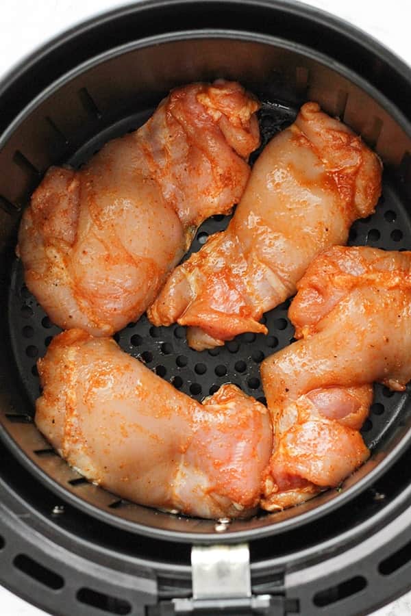 chicken thighs in an air fryer basket.