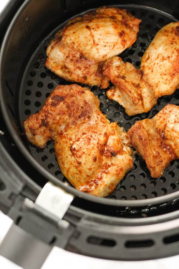 cooked chicken thighs in an air fryer basket.